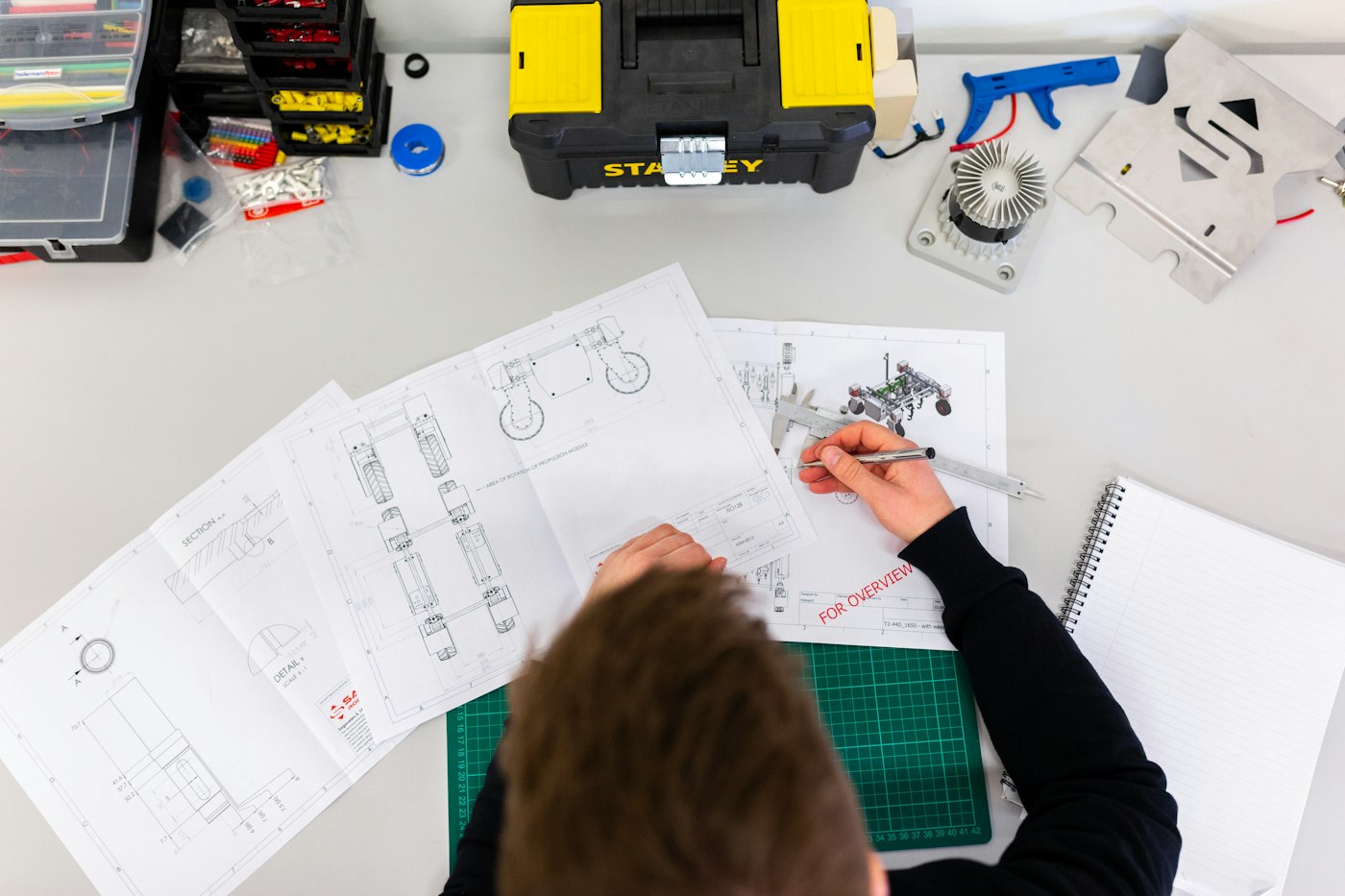 Hands drawing technical sketches on paper beside tools